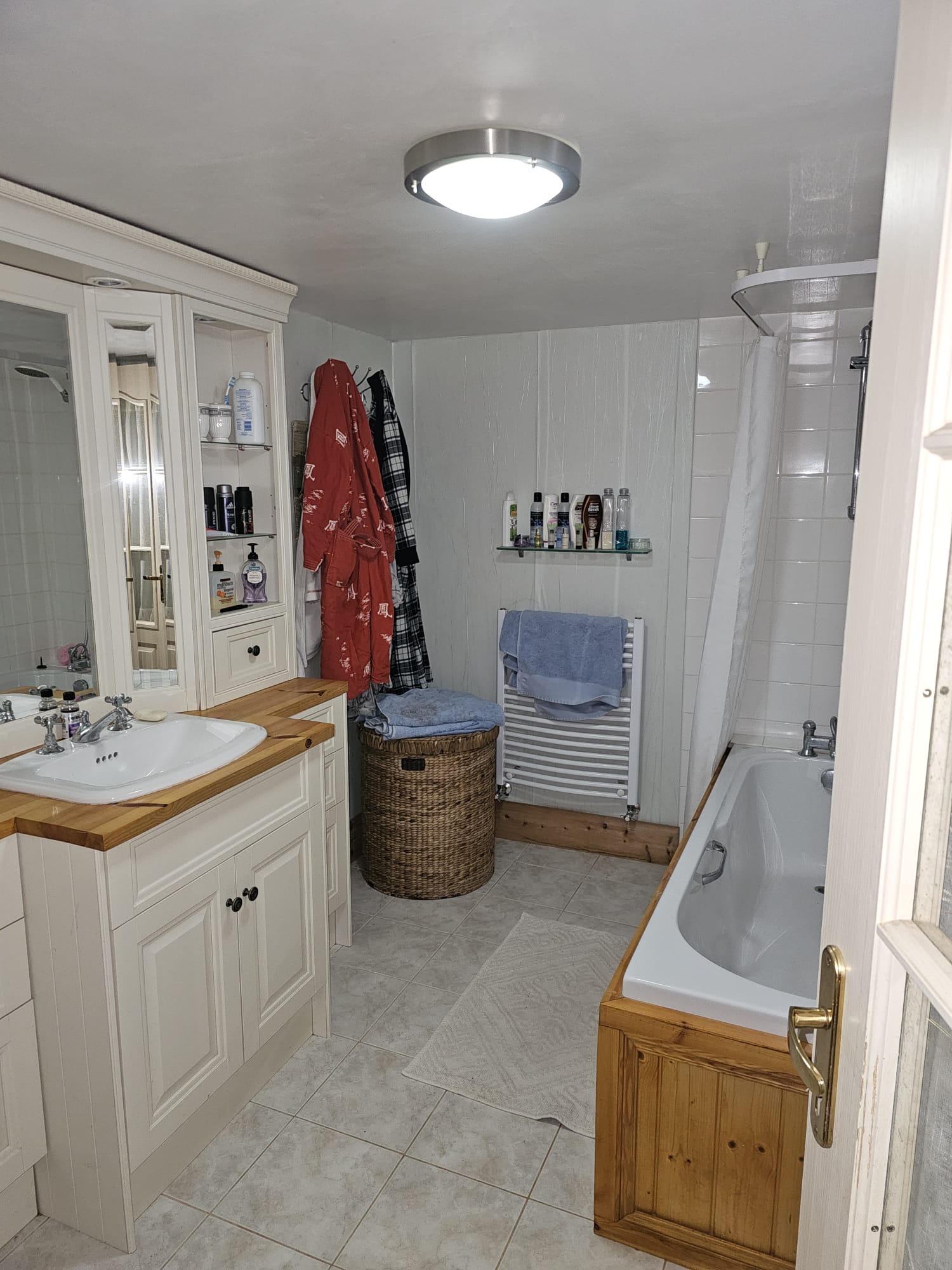 A cottage bathroom with cream cabinetry, wooden bath surround and tile floor
